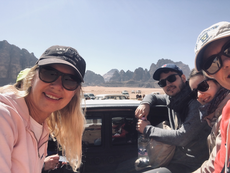 Group of people smiling with cliffs and sky in the background.