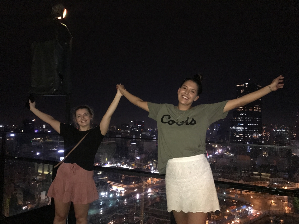Deux personnes avec les bras levés, paysage urbain nocturne en arrière-plan.
