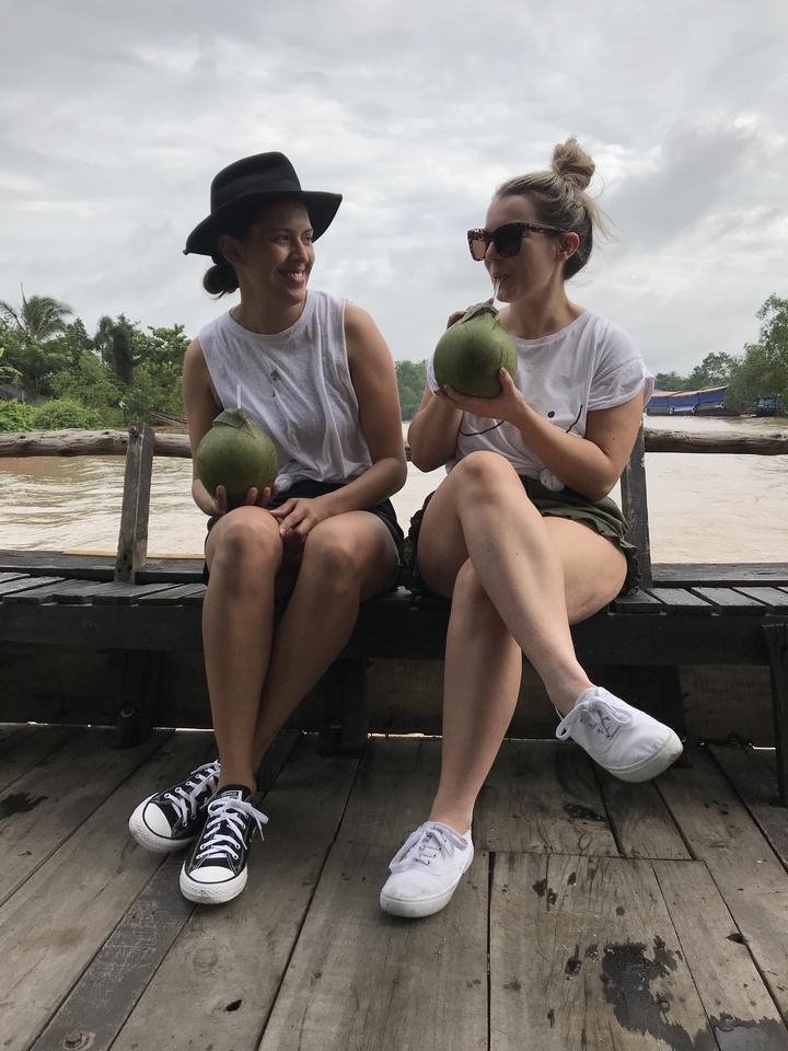 Deux personnes tenant des noix de coco, assises sur un banc en bois au bord de l'eau.