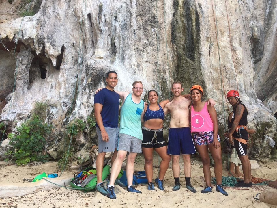Groupe de personnes dans une zone d'escalade sur rocher à la plage, souriant devant les falaises.