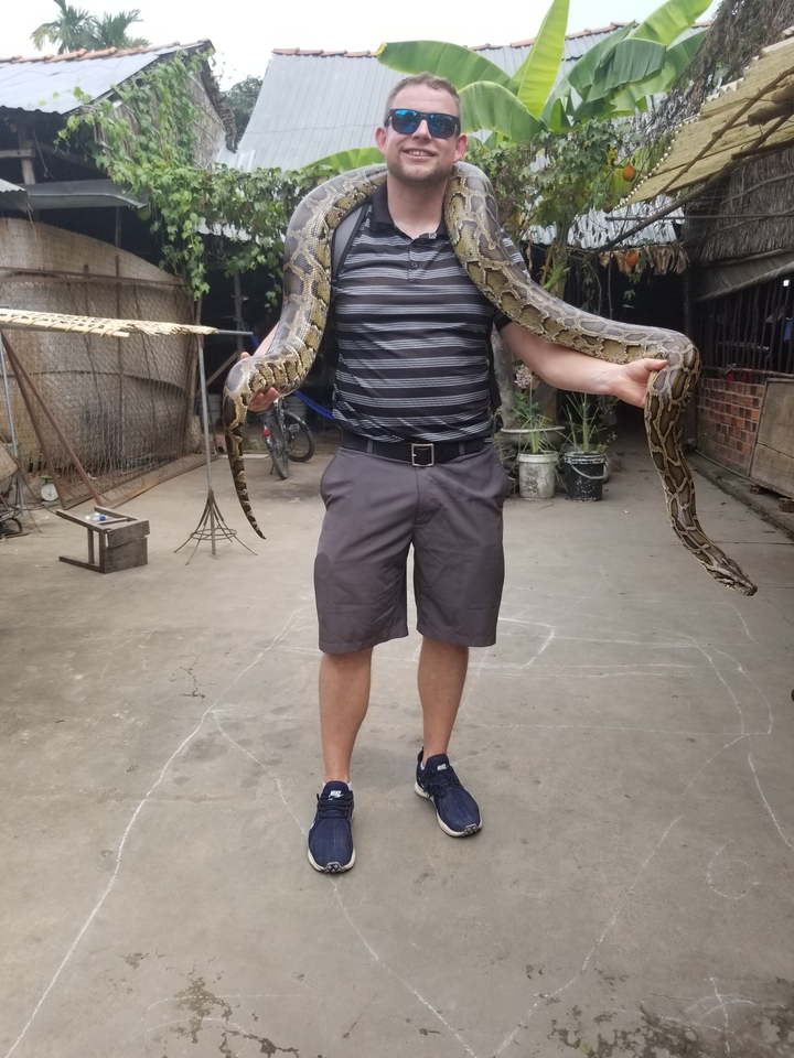 Personne tenant un grand serpent dans une cour.