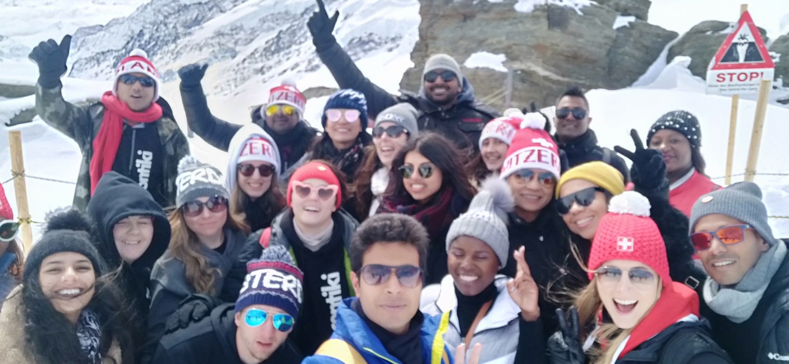 Grand groupe de personnes posant sur une montagne enneigée avec des bonnets « Suisse ».