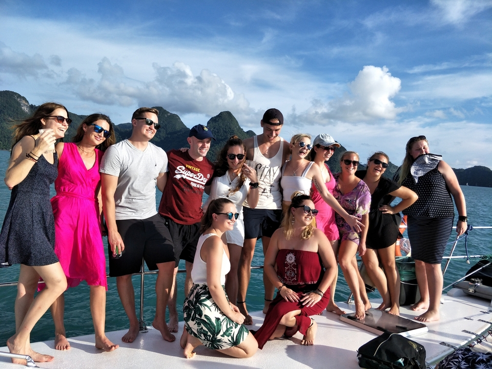 Groupe posant sur un bateau avec des collines en arrière-plan.