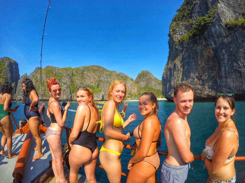 Group of friends posing on a boat with scenic cliffs.