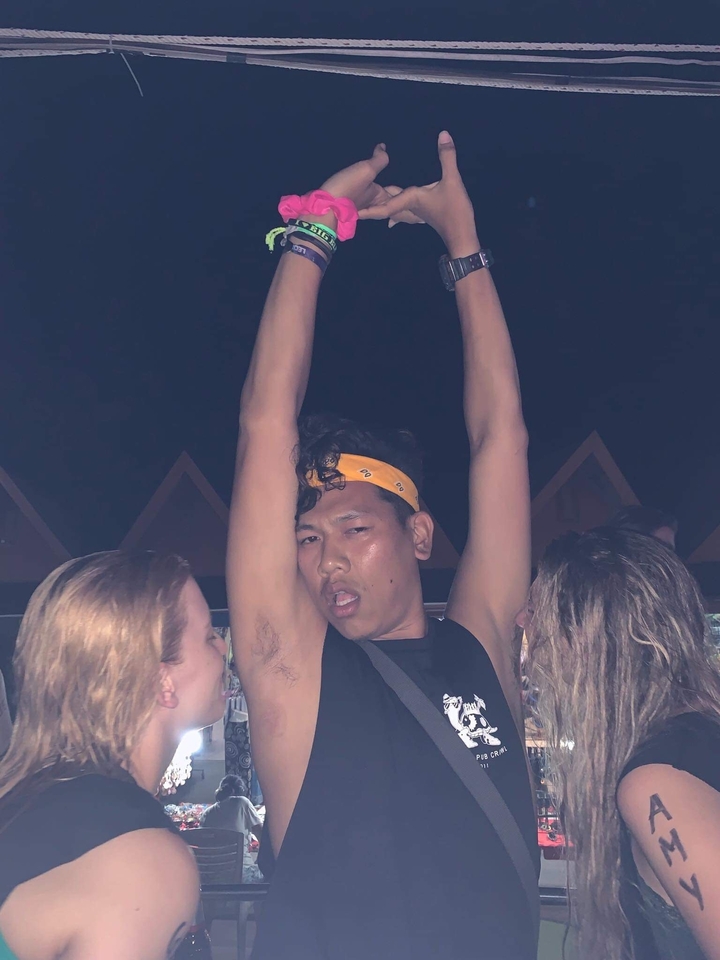 Person raising hands in a social setting, with others visible in the background.