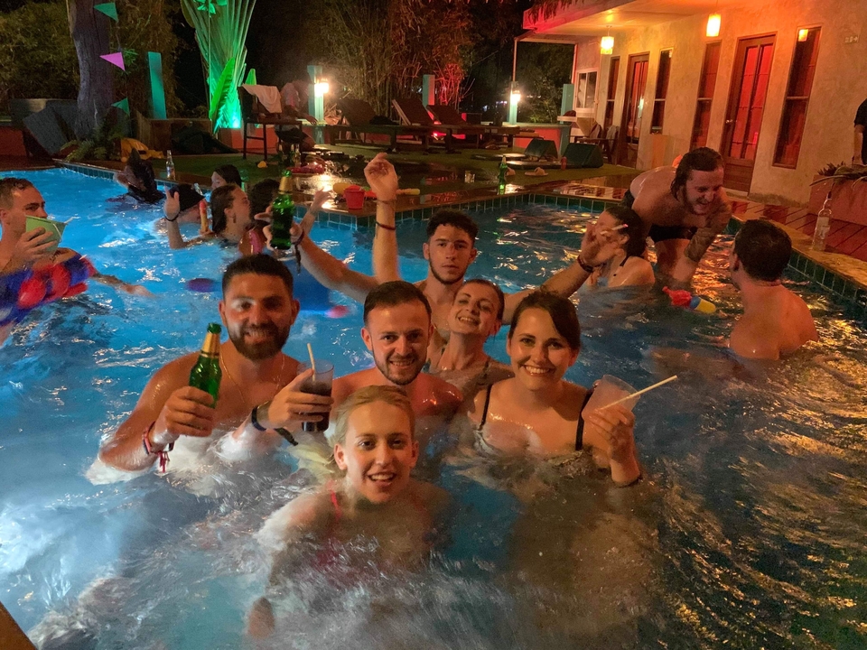 Group of friends enjoying a pool party at night with drinks.