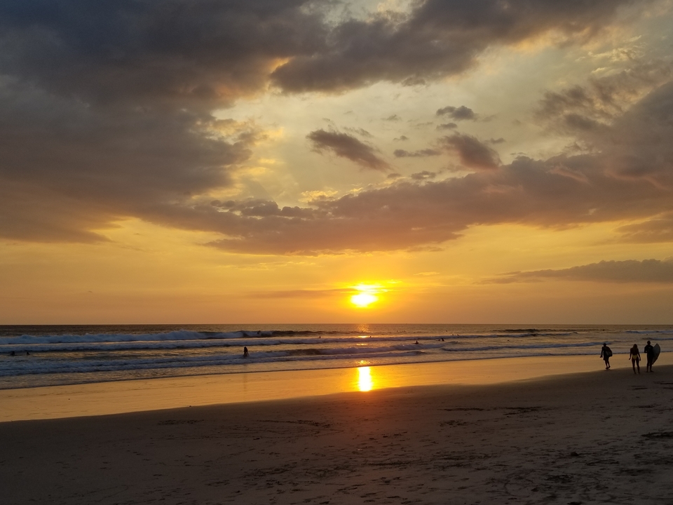 Une plage au coucher du soleil avec des gens qui se promènent le long du rivage.