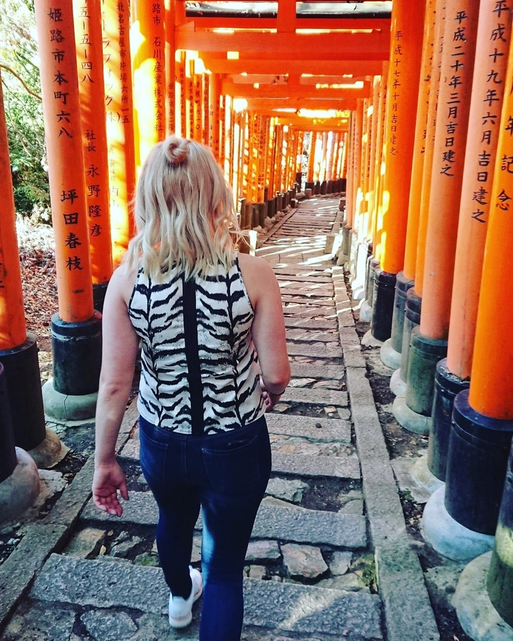 Vue de dos d'une femme marchant à travers des torii rouges.