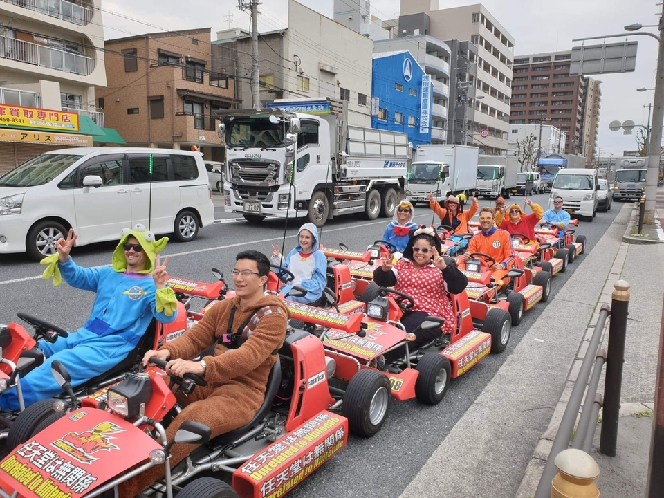 Groupe de personnes en costumes conduisant des karts dans une rue.