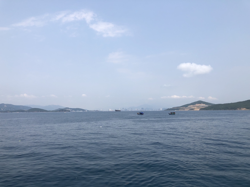 Vue panoramique d'une mer calme avec des collines lointaines sous un ciel dégagé.