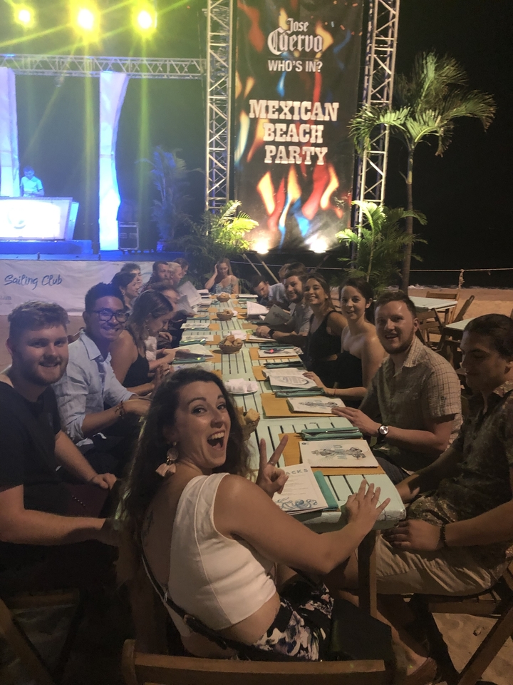 Groupe de personnes assises à une longue table dans un restaurant en plein air.