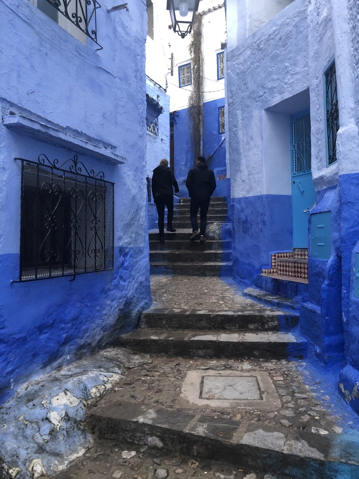 Deux personnes montant des escaliers peints en bleu dans une ruelle étroite.