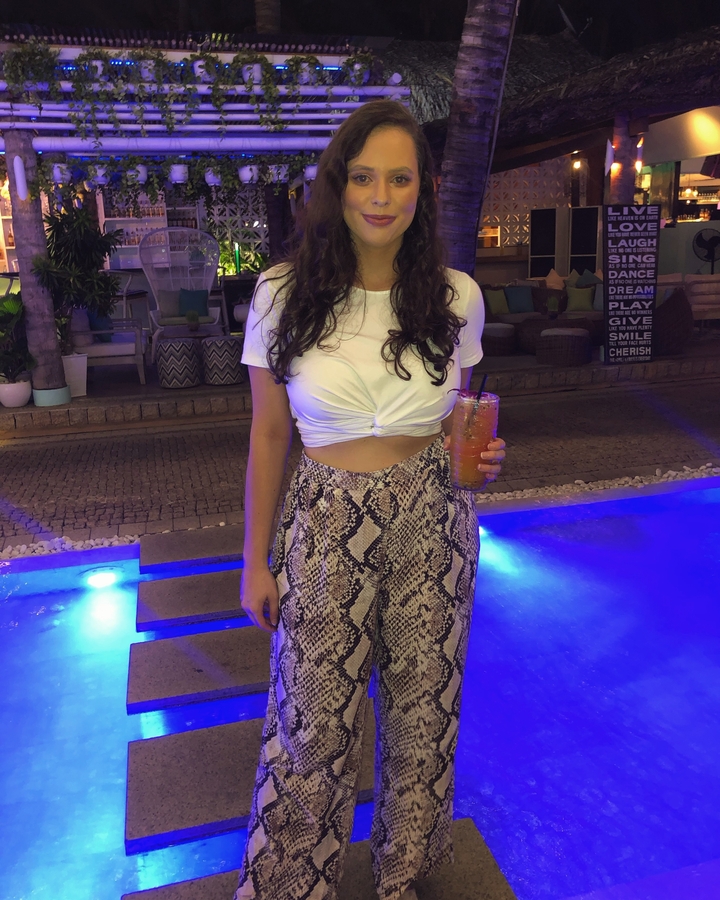 Personne debout avec une boisson au bord d'une piscine la nuit.