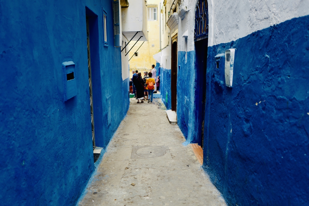 Des gens qui marchent dans une ruelle bleue étroite.