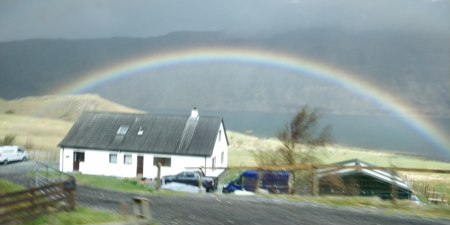 A house with a rainbow in a rural landscape.