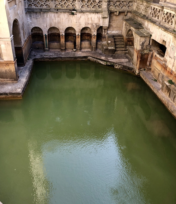 Thermes romains avec une eau de couleur olive et des structures anciennes.