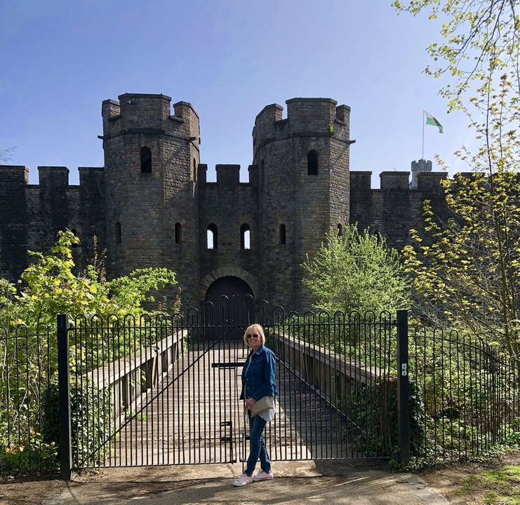 Porte de château avec une femme debout à l'entrée, drapeau visible en arrière-plan.
