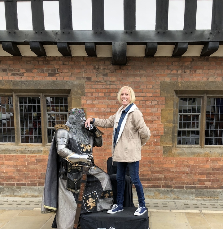 Woman standing next to a knight statue in armor with a brick building backdrop.