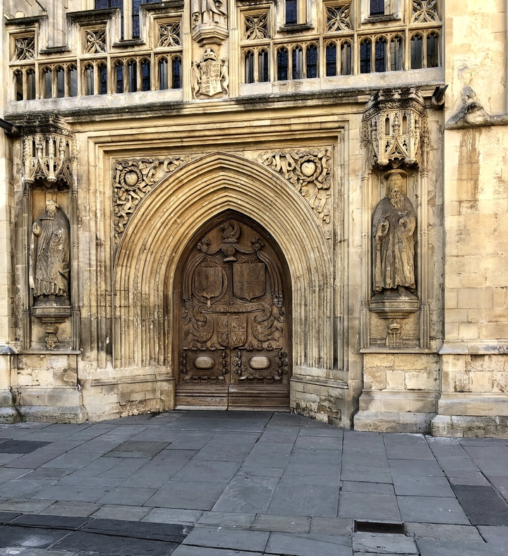 Porte en bois ornée flanquée de deux statues, sculptures détaillées visibles.