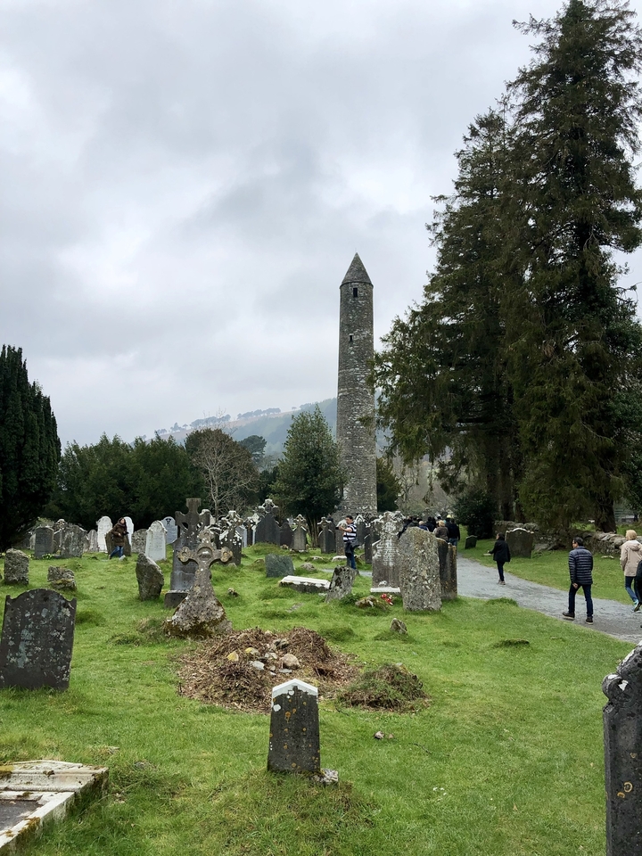 Ancient graveyard with a round tower and people walking.
