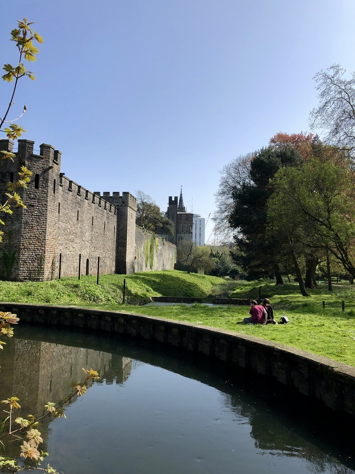Castle wall with a garden and people sitting on the grass.