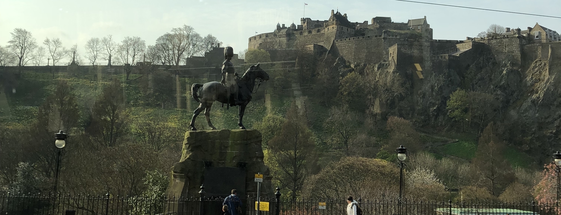 Statue of a horseman in front of a castle with people walking by.