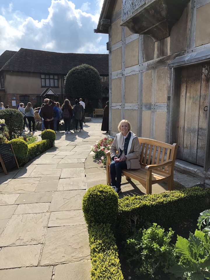Woman sitting on a bench in a garden with a group of people around.