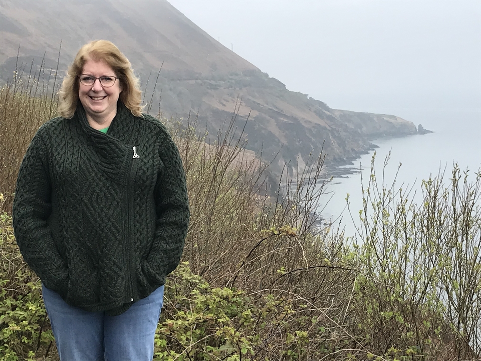 Femme en pull posant près d'un littoral brumeux.