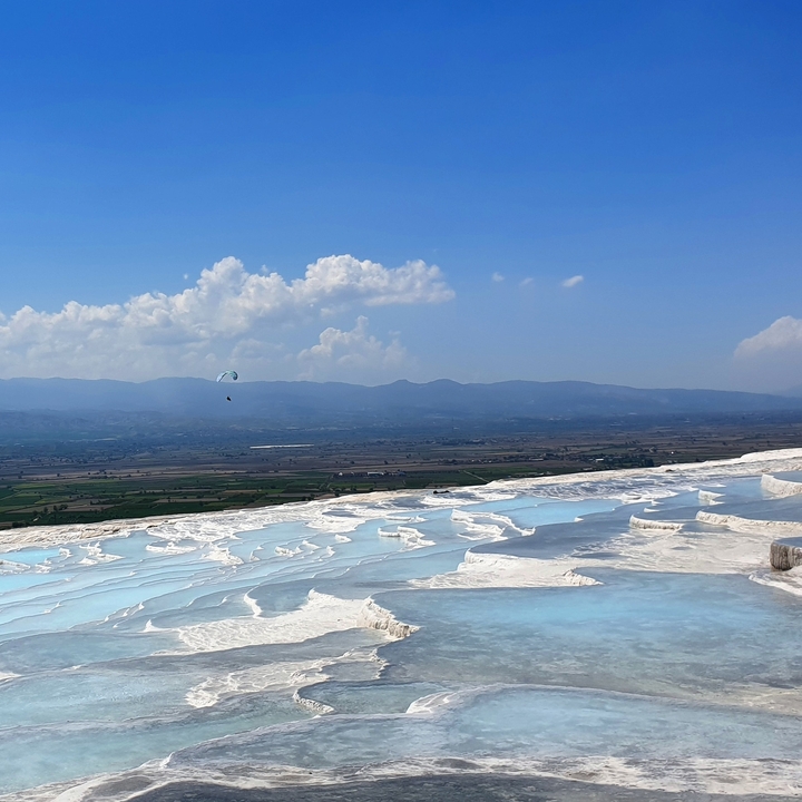Terrasses de travertin blanc avec un parapentiste dans le ciel.