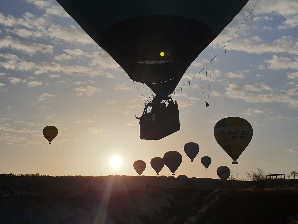 Montgolfières s'élevant au lever du soleil dans un paysage rocheux.