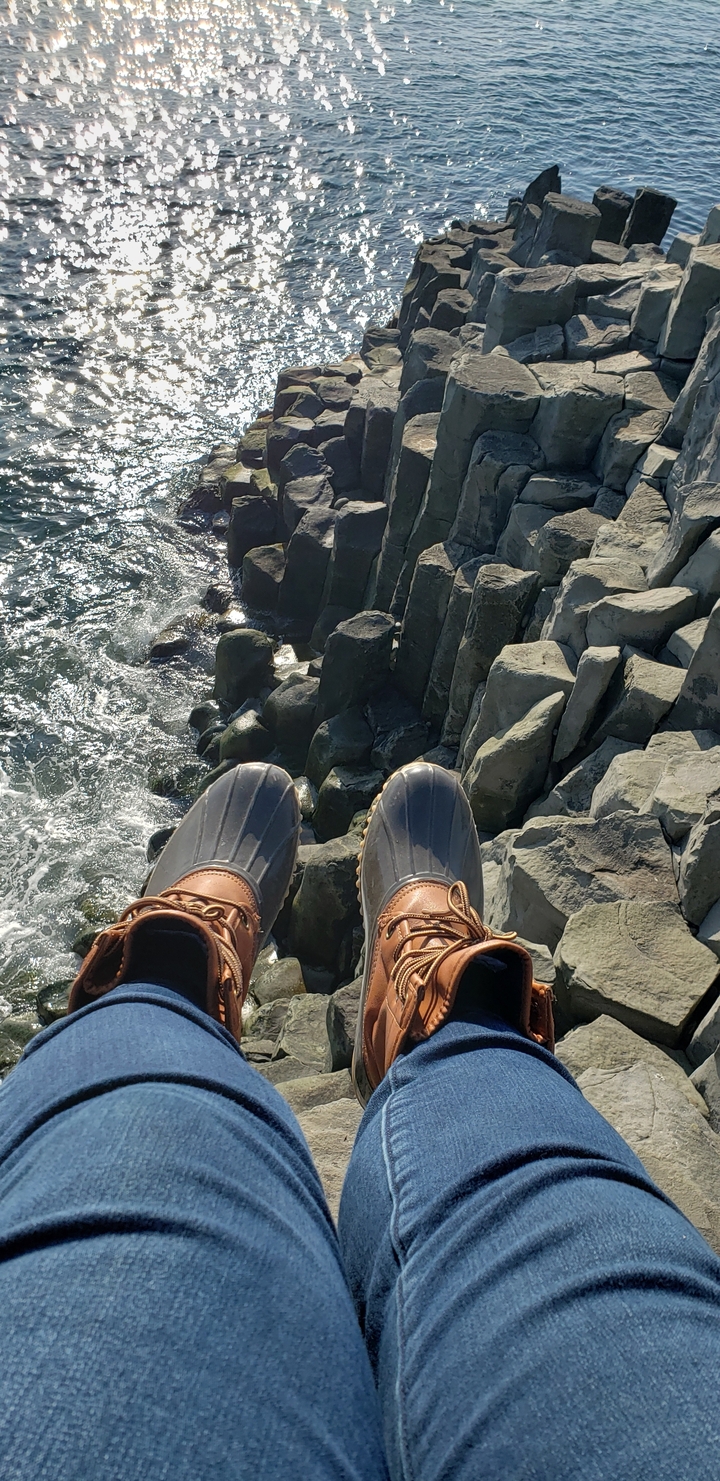 Feet in boots dangled over rocky coastline.