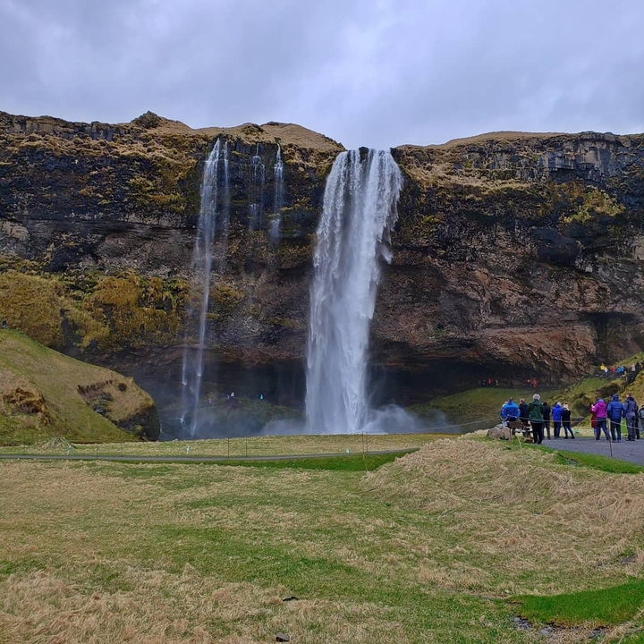 Tall waterfall cascading over cliffs with visitors nearby.