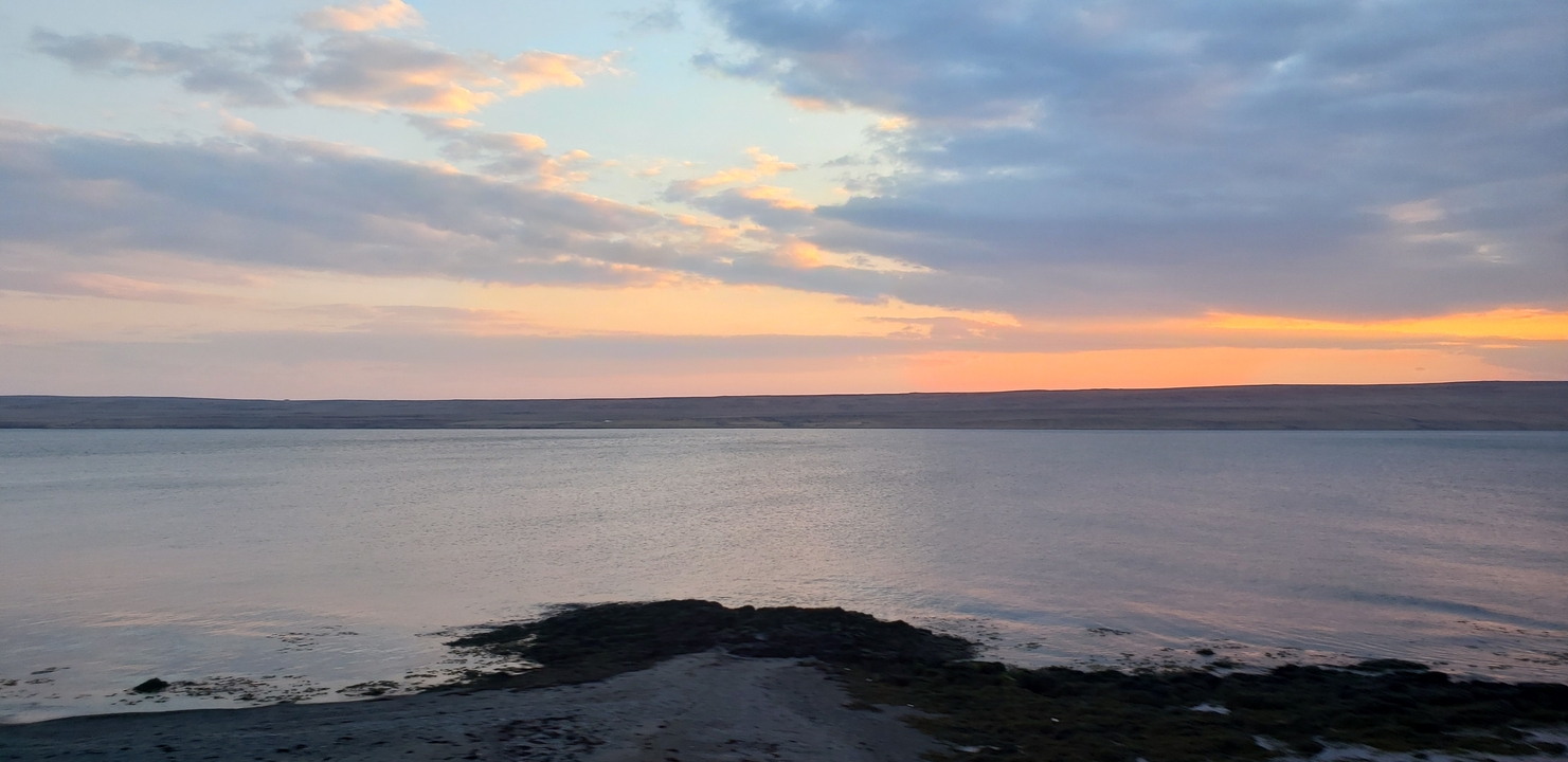 Calm ocean at sunset with clouds and serene water.