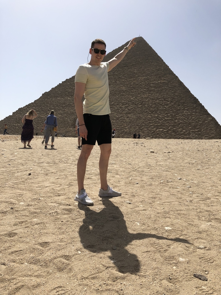 Personne debout devant une pyramide, avec d'autres qui marchent à proximité.