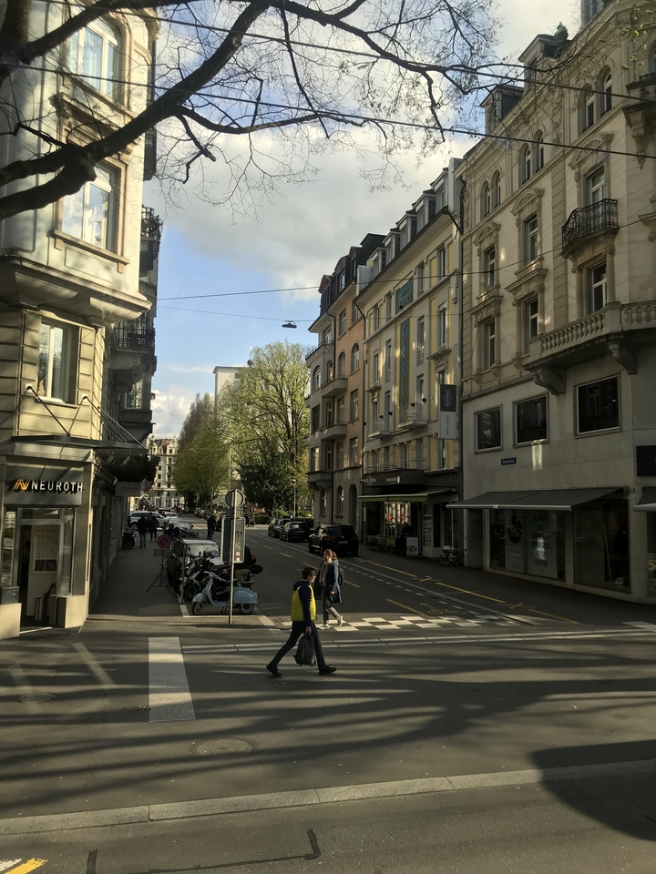 Scène de rue avec des gens qui marchent et bordée de bâtiments.