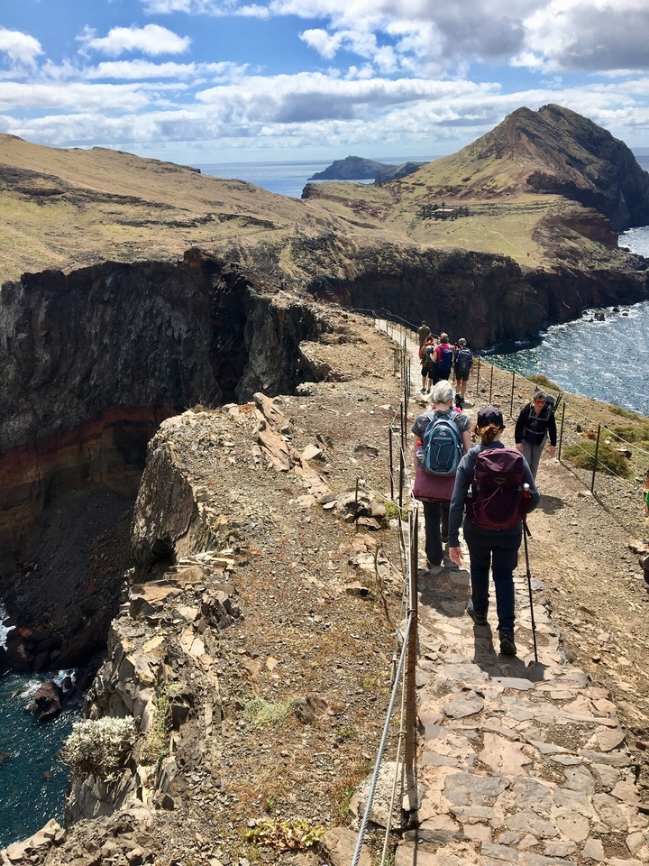 Randonneurs marchant le long d'une falaise rocheuse avec vue sur l'océan.