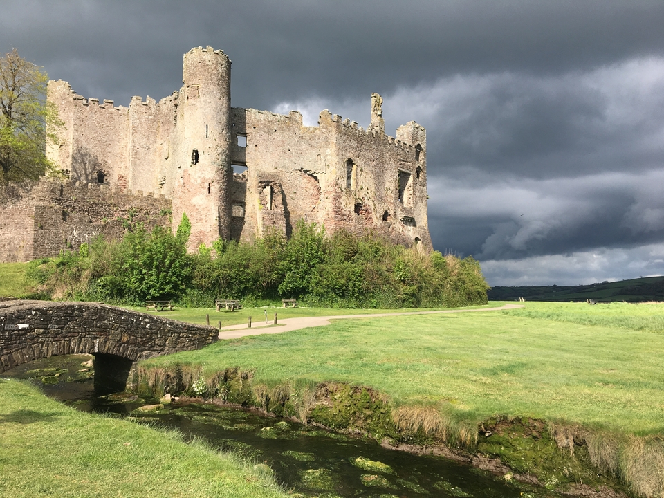 Château en ruines sur un paysage herbeux sous des nuages sombres.