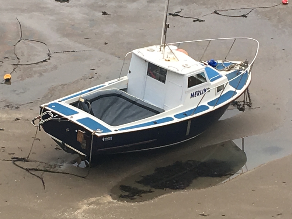 Petit bateau nommé Merlin sur une rive boueuse.