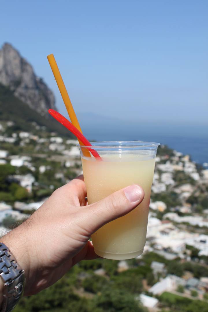 Hand holding a drink with a coastal view in the background.