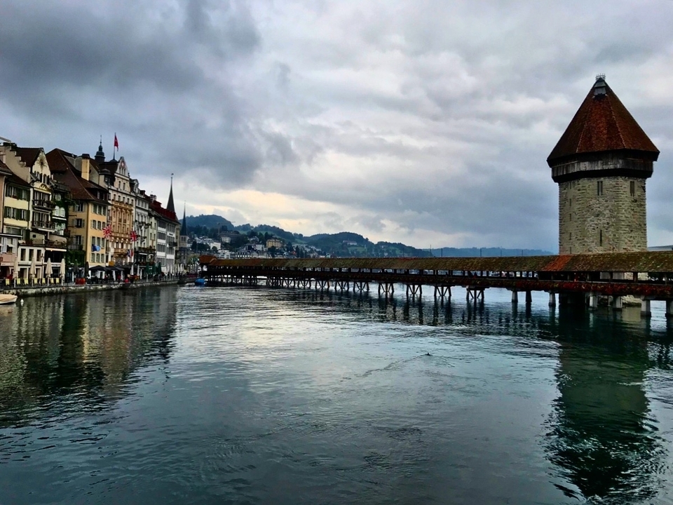 Historic wooden Chapel Bridge and water tower span the Reuss River in Lucerne under moody skies.