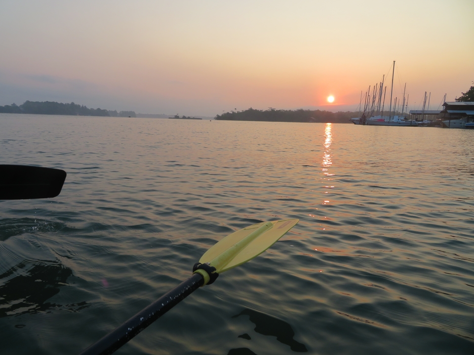 Pagaie de kayak dans l'eau au coucher du soleil avec des bateaux au loin.