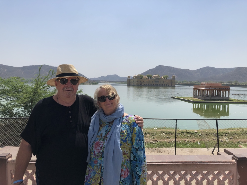 Couple debout au bord d'un lac avec une vue lointaine du Jal Mahal.