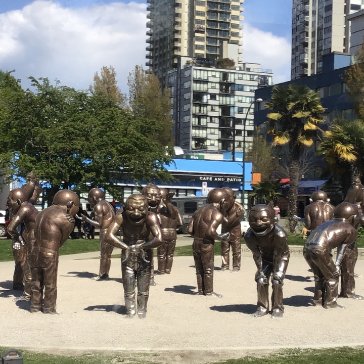 Parc de sculptures avec des statues expressives et des bâtiments urbains.