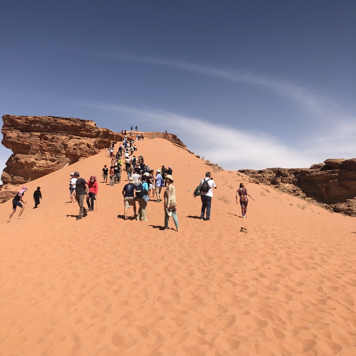 Group of tourists climbing a sand dune with a rocky outcrop in the background