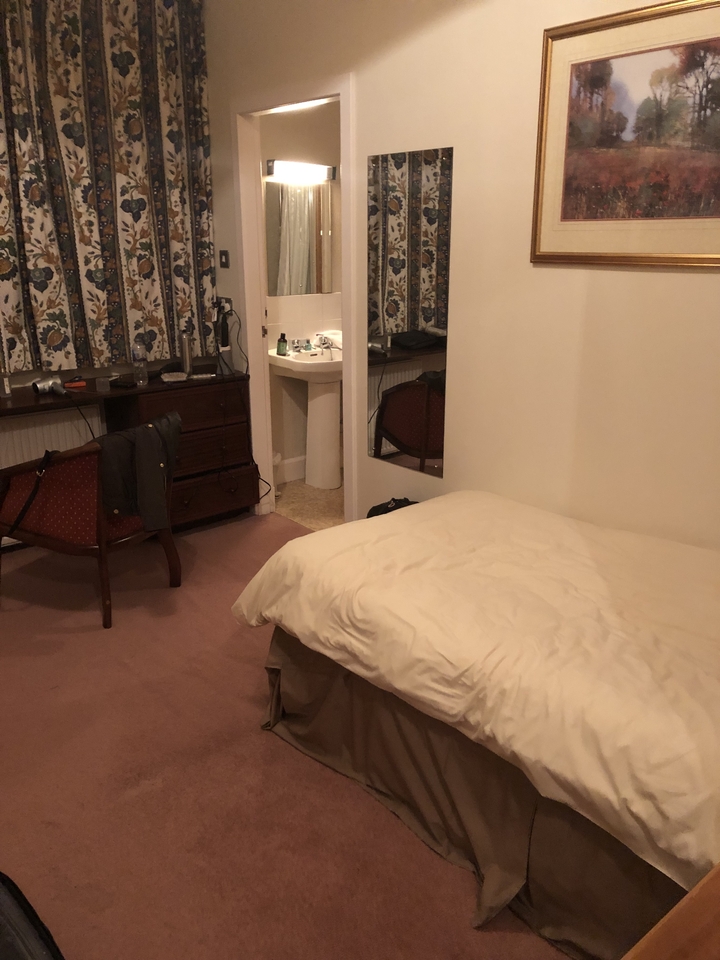 Intérieur d'une chambre à coucher avec un lit, une chaise et une commode.