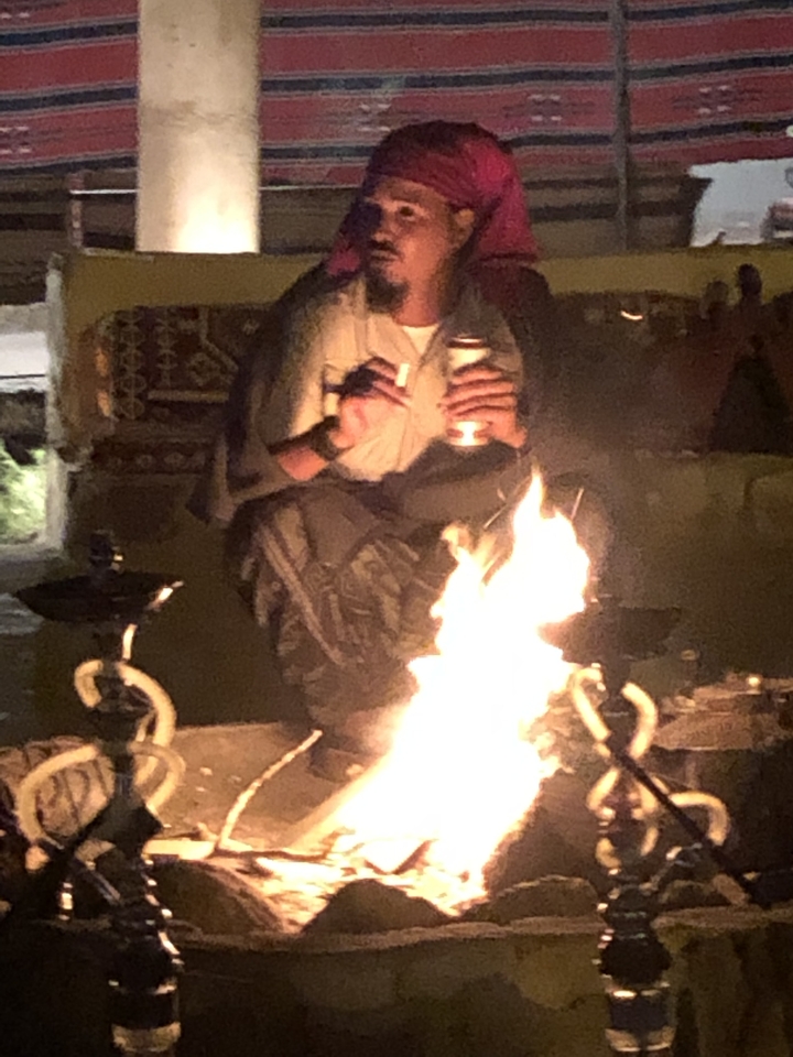 Personne assise près d'un feu de camp dans une zone faiblement éclairée.