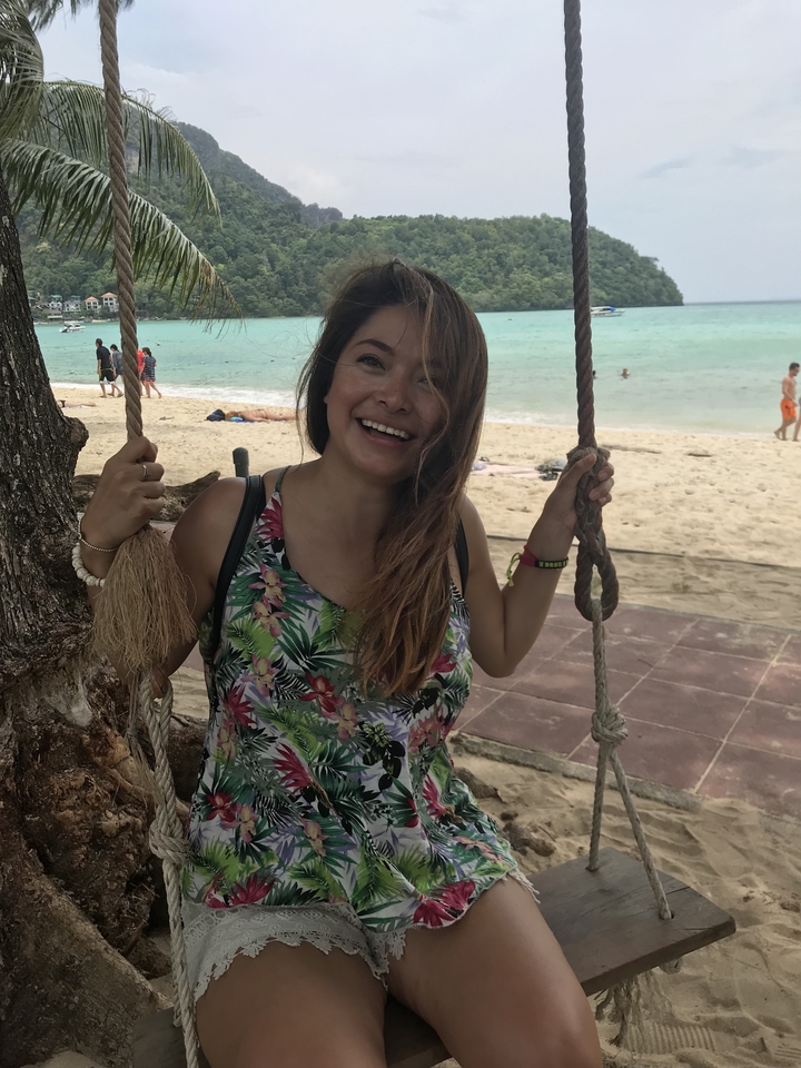 Person swinging from a tree with a beach and ocean in the background.