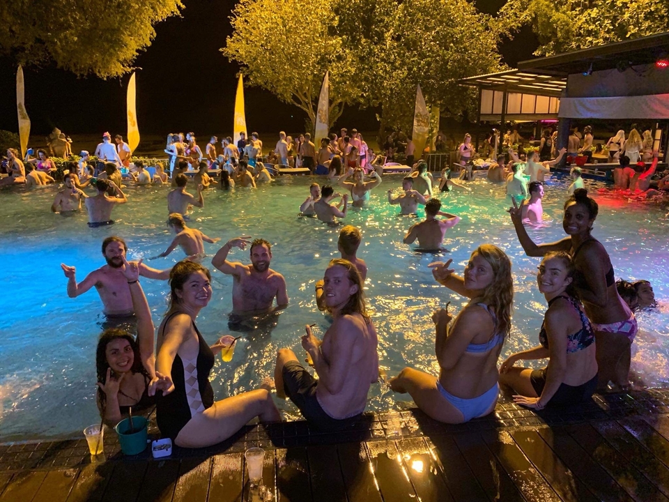 Poolside scene with people enjoying a party with colorful lights.