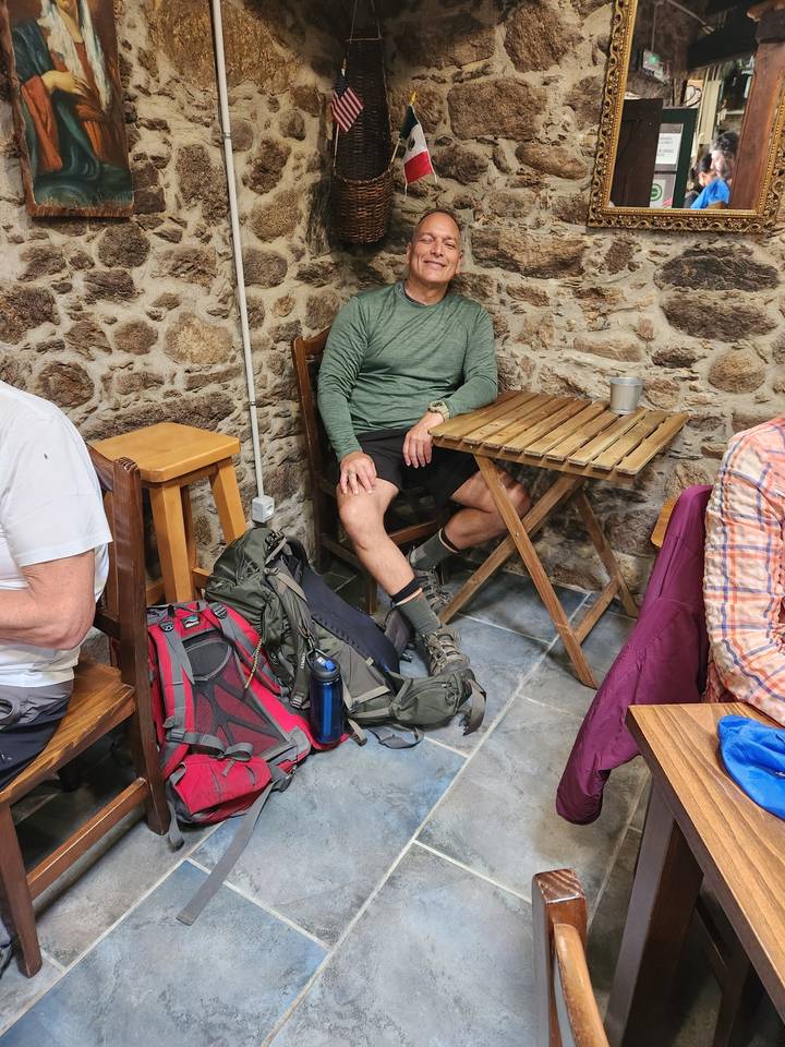 Homme assis à un café avec un sac à dos et des bâtons de randonnée.