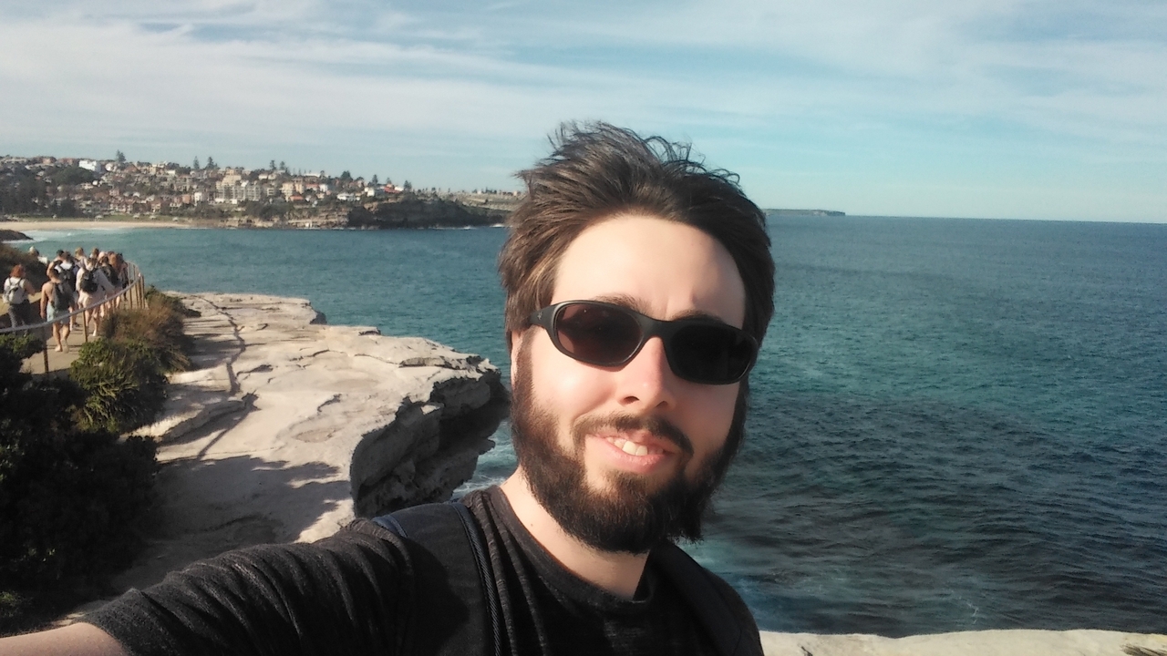Person taking a selfie with a coastal view in the background.